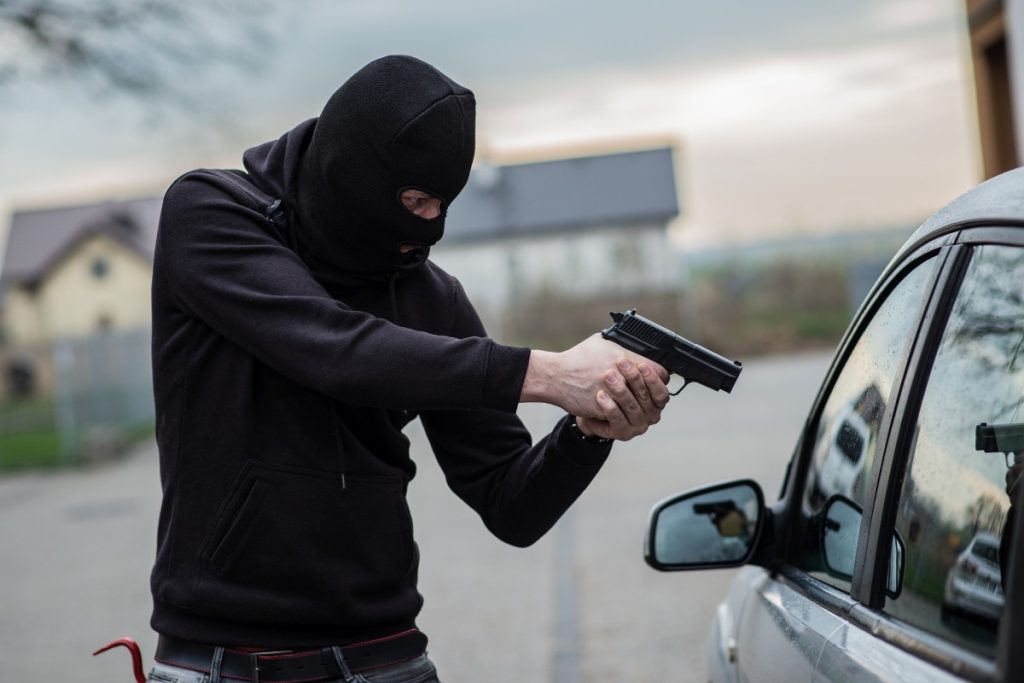 Homem com arma e gorro preto no rosto assaltando carro