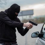 Homem com arma e gorro preto no rosto assaltando carro