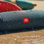 Caixa de som JBL preta com gotas de água sobre superfície molhada na praia