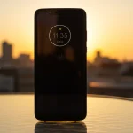 Fx Motorola Moto G75 positioned vertically on a glass table with city skyline blurred in the background during golden hour 1