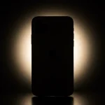 Fx iPhone 16e with dramatic backlighting creating halo effect silhouette style with subtle details visible artistic product photography approach 3